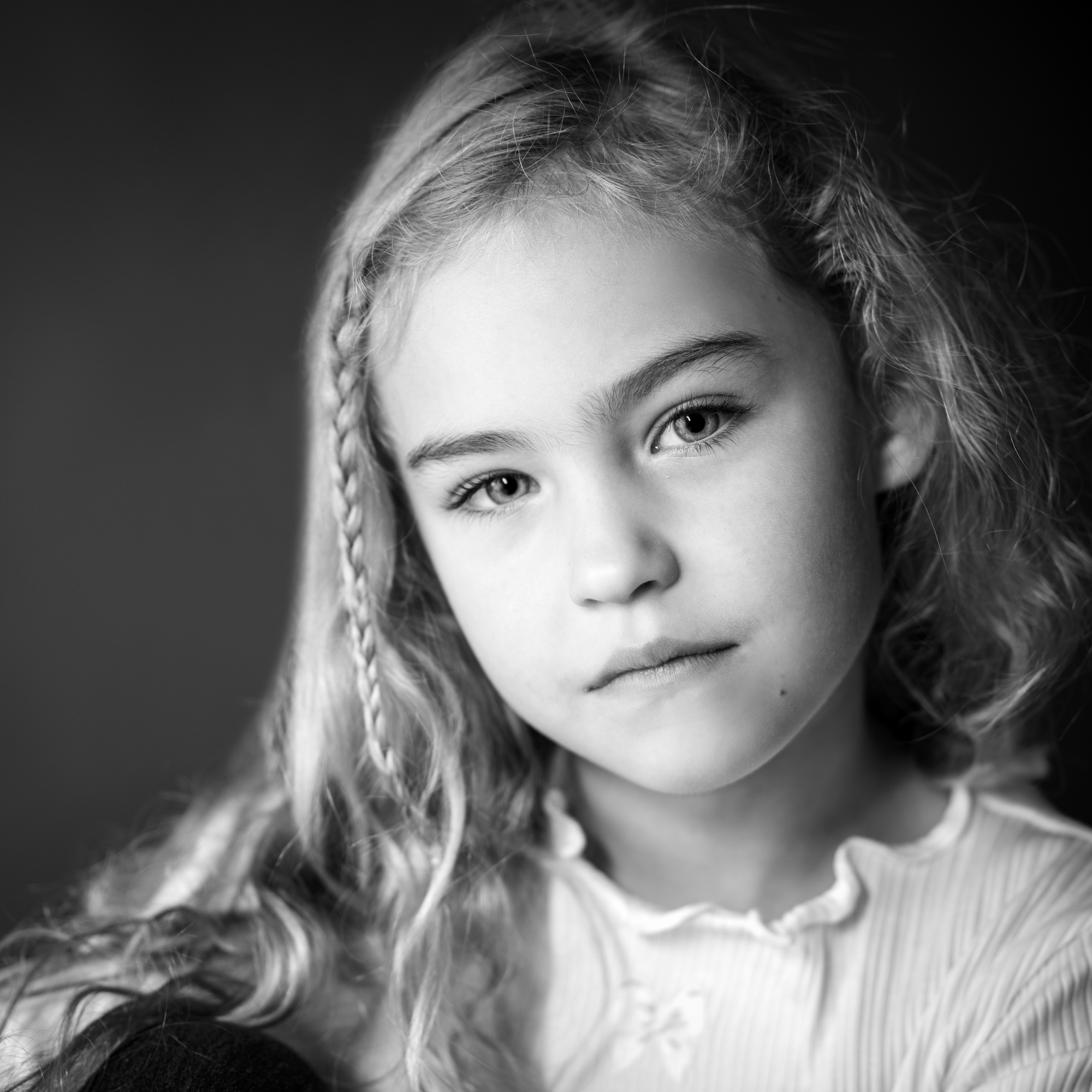 Black-and-white portrait of a young girl with long, wavy blonde hair and a soft, introspective gaze, by Jerome Art Photography.