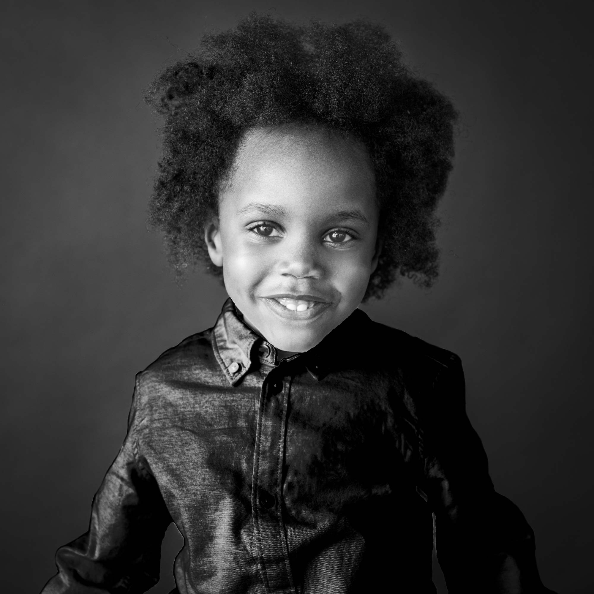 Black-and-white portrait of a smiling young child with natural afro hair, wearing a buttoned shirt, by Jerome Art Photography.