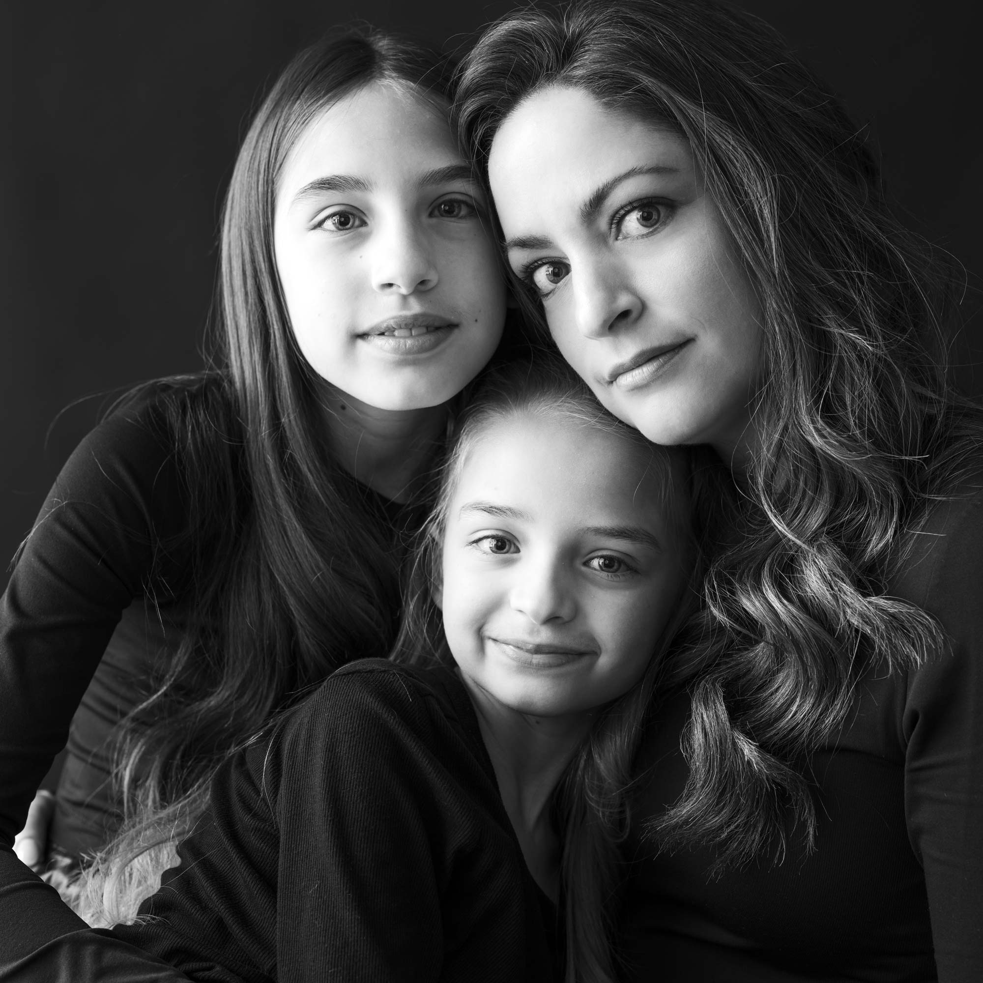 Black-and-white portrait of a mother with her two daughters, all wearing black, in a close embrace, by Jerome Art Photography.